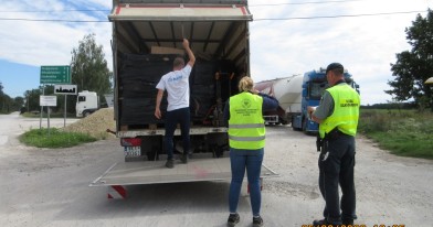 Inspektorzy Ochrony Środowiska oraz pracownik służby celno- skarbowej w trakcie kontroli ciężarówki w której są palety opakowaniami kartonowymi.