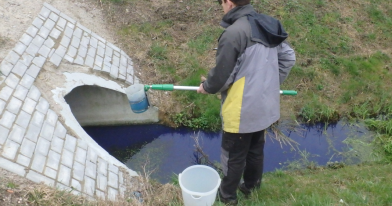 Próbobiorca nad brzegiem rzeki po pobraniu próbki wody