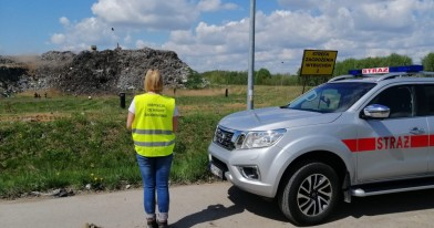 Pracownik Inspekcji Ochrony Środowiska na tle palącej się hałdy odpadów