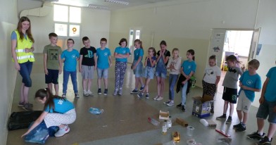 Dzieci z Inspektorem Wojewódzkiego Inspektoratu Ochrony Środowiska podczas zabaw edukacyjny na korytarzu szkolnym.