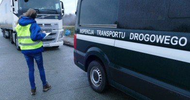 Pani Inspektor Ochrony Środowiska stoi pomiędzy autem służbowym Inspekcji Transportu Drogowego a zatrzymanym Tirem do kontroli, sporządza notatkę służbową