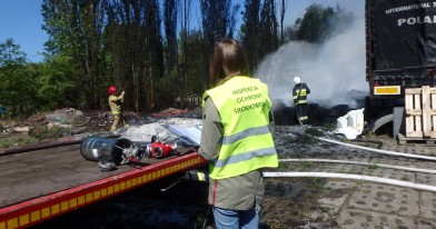 Inspektor WIOŚ w Łodzi na tle strażaków dogaszających palące się opony