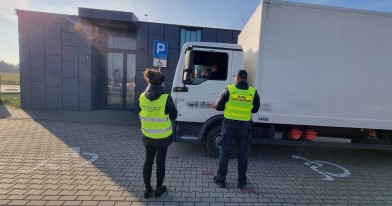 Inspektor WIOŚ oraz funkcjonariusz Służby Celno-Skarbowej stojący na przeciwko białego busa, prowadząc czynności kontrolne.