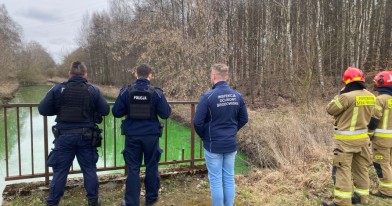Funkcjonariusze Policji i Państwowej Straży Pożarnej wraz z przedstawicielem Inspekcji Ochrony Środowiska przy rzece.