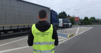Inspektor Ochrony Środowiska, stojący przy naczepie zatrzymanego  ciągnika siodłowego, podczas czynności kontrolnych