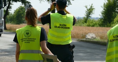 Pani Inspektor Ochrony Środowiska wraz z funkcjonariuszem Służby Celno Skarpowej stoją przy trasie i typują przez lornetkę pojazd do kontroli