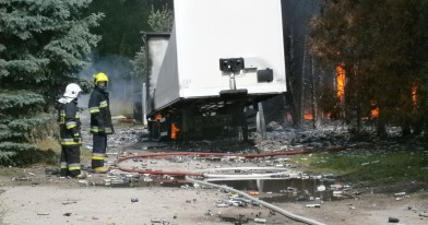 Na pierwszym planie funkcjonariusze straży pożarnej podczas czynność gaśniczych w tle nadpalona przyczepa ciągnika siodłowego