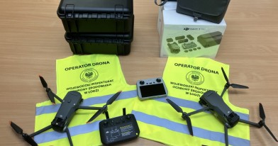 dwa drony wraz z oprzyrządowaniem, wyeksponowane na odblaskowych kamizelkach z napisem operator drona